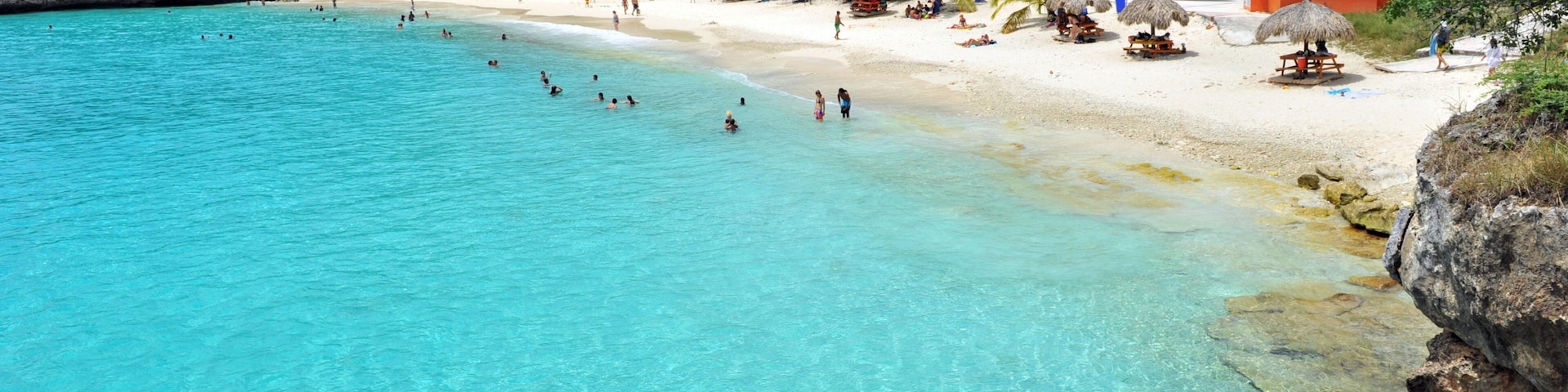 A turquoise beach with clear water, white sand, and lush green hills in the background.