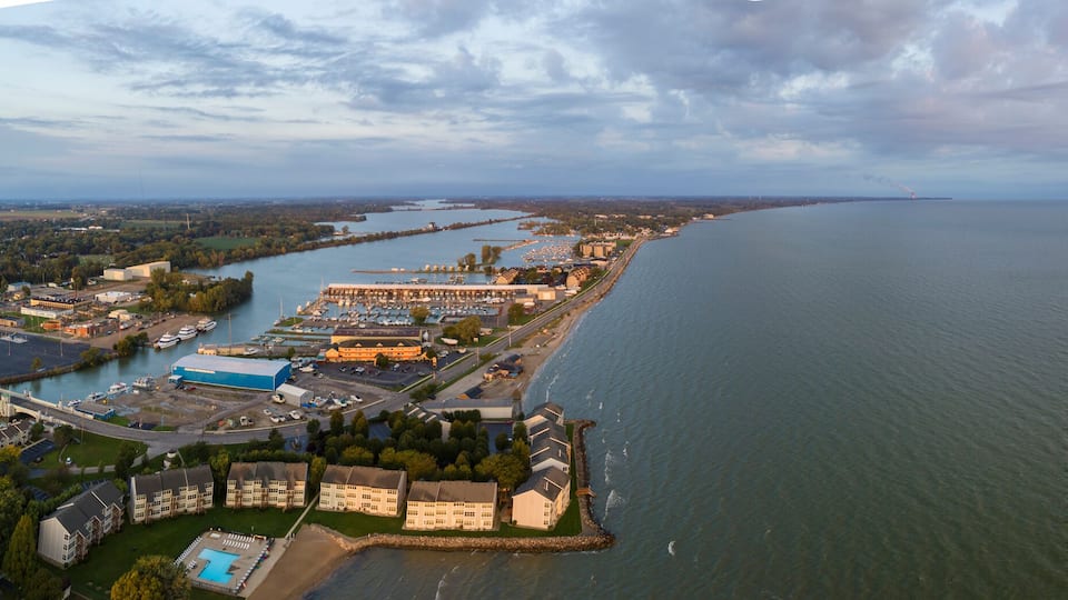 An aerial view of a coastal city with a marina, industrial buildings, and a large body of water.