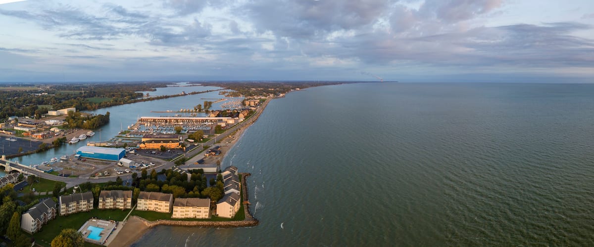 An aerial view of a coastal city with a marina, industrial buildings, and a large body of water.