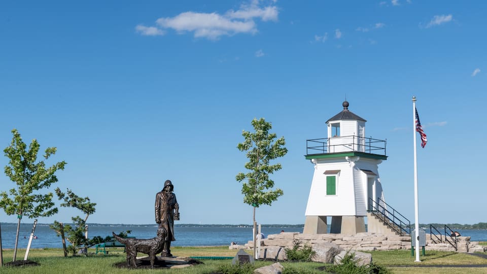 A lighthouse, a statue, and a flag by a body of water.