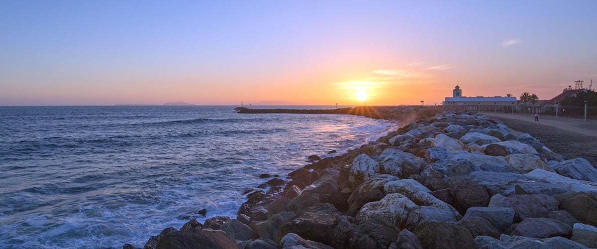 A rocky shoreline with a lighthouse at sunset.