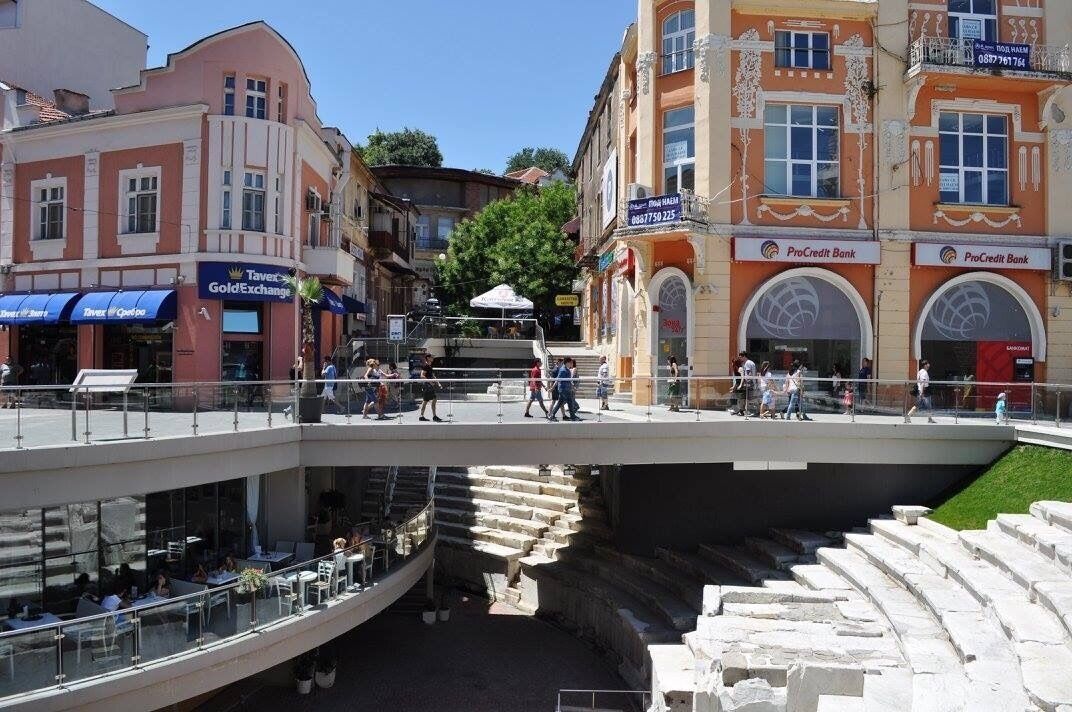Un puente peatonal flanqueado por comercios y una sucursal del banco ProCredit.