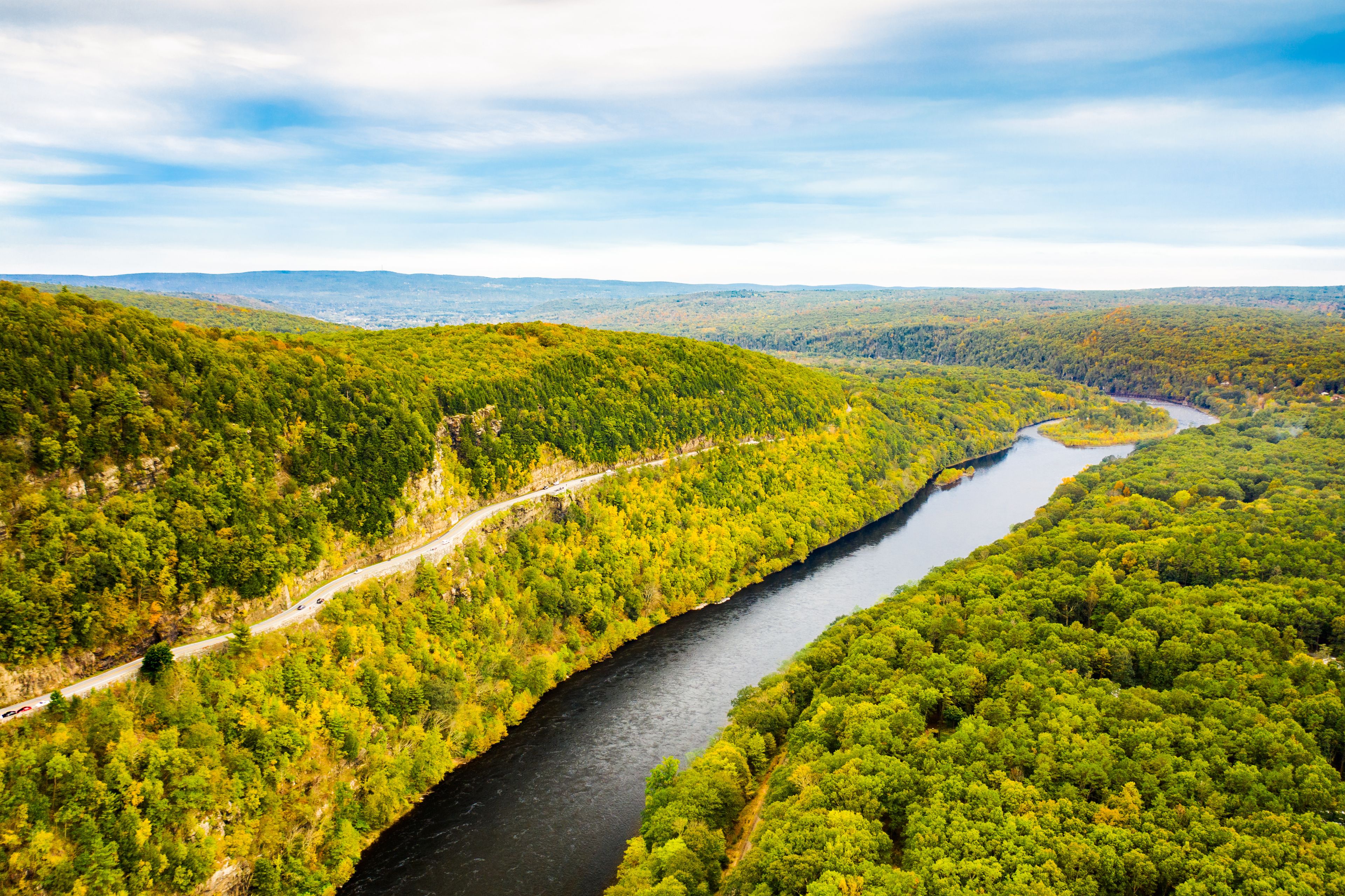 A river winding through a densely forested valley with a road running alongside it.