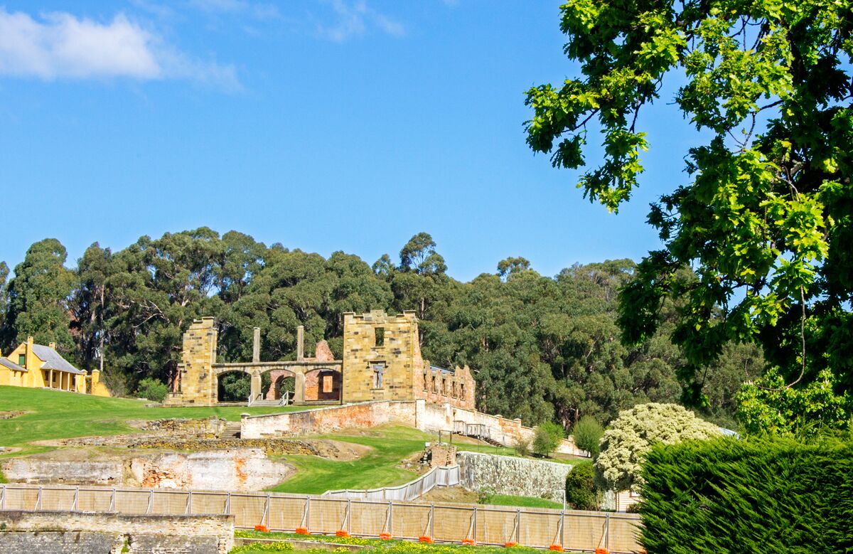 An ancient stone structure with arches and ruins, surrounded by lush green trees and a clear blue sky.