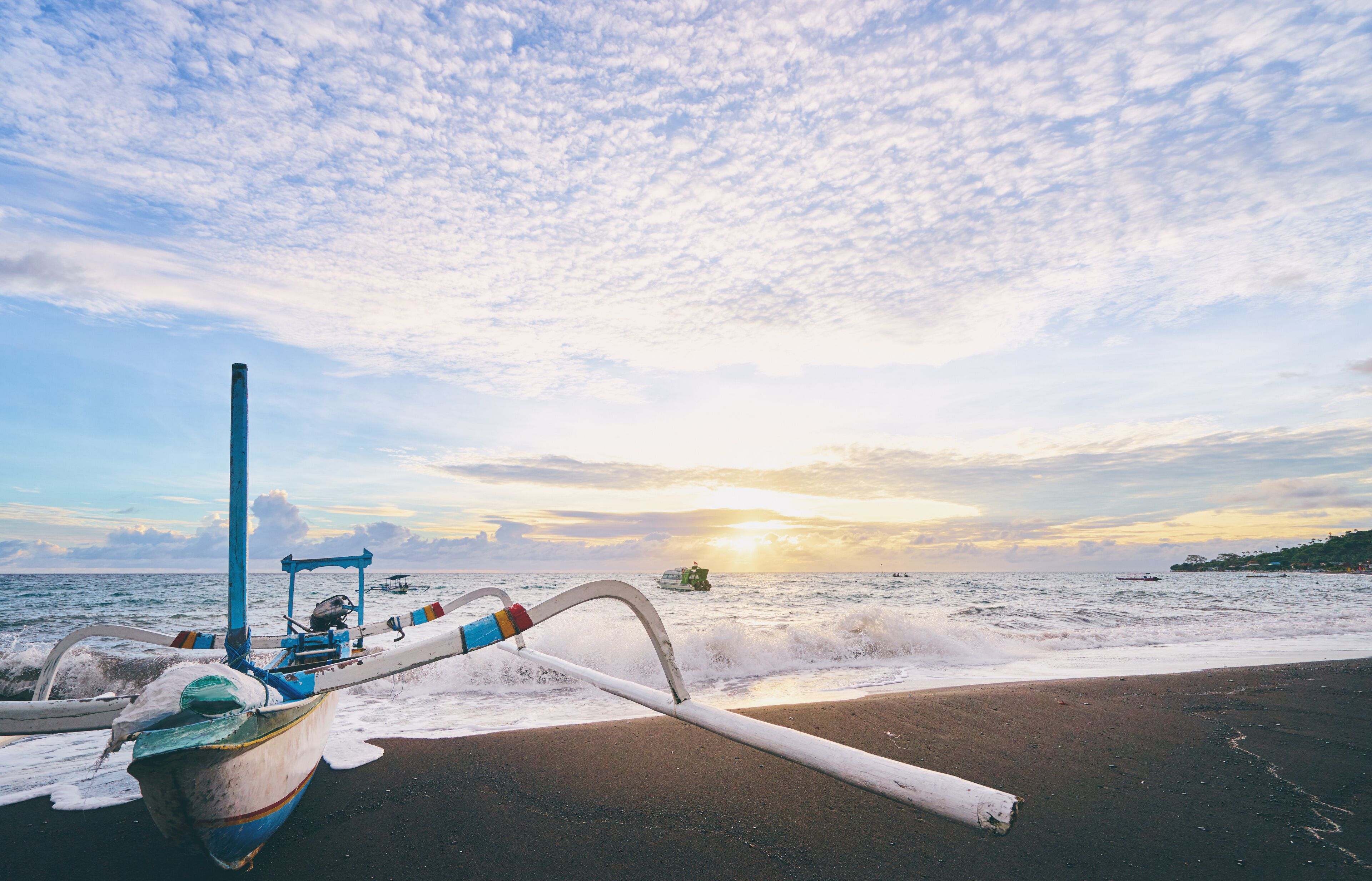 A boat on a beach with the ocean and a sunset in the background.