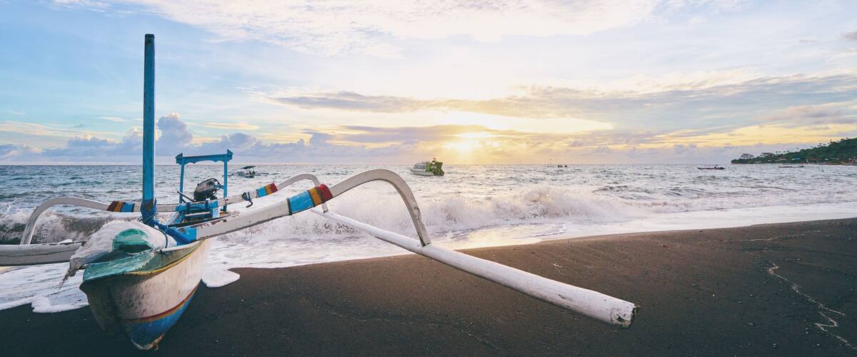 A boat on a beach with the ocean and a sunset in the background.