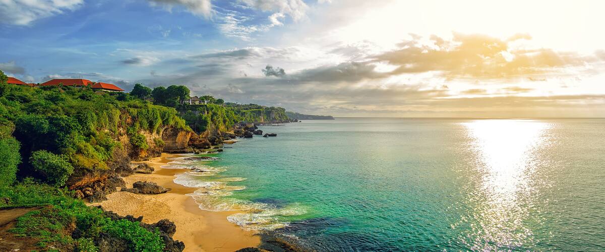 A coastal landscape with a sandy beach, rocky cliffs, and a clear view of the ocean.