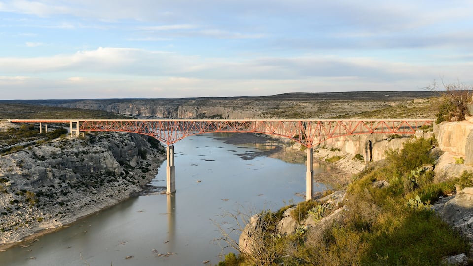 A red bridge over a river with rocky banks and sparse vegetation.