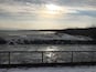 A frozen river with a fence in the foreground and birds flying in the sky.