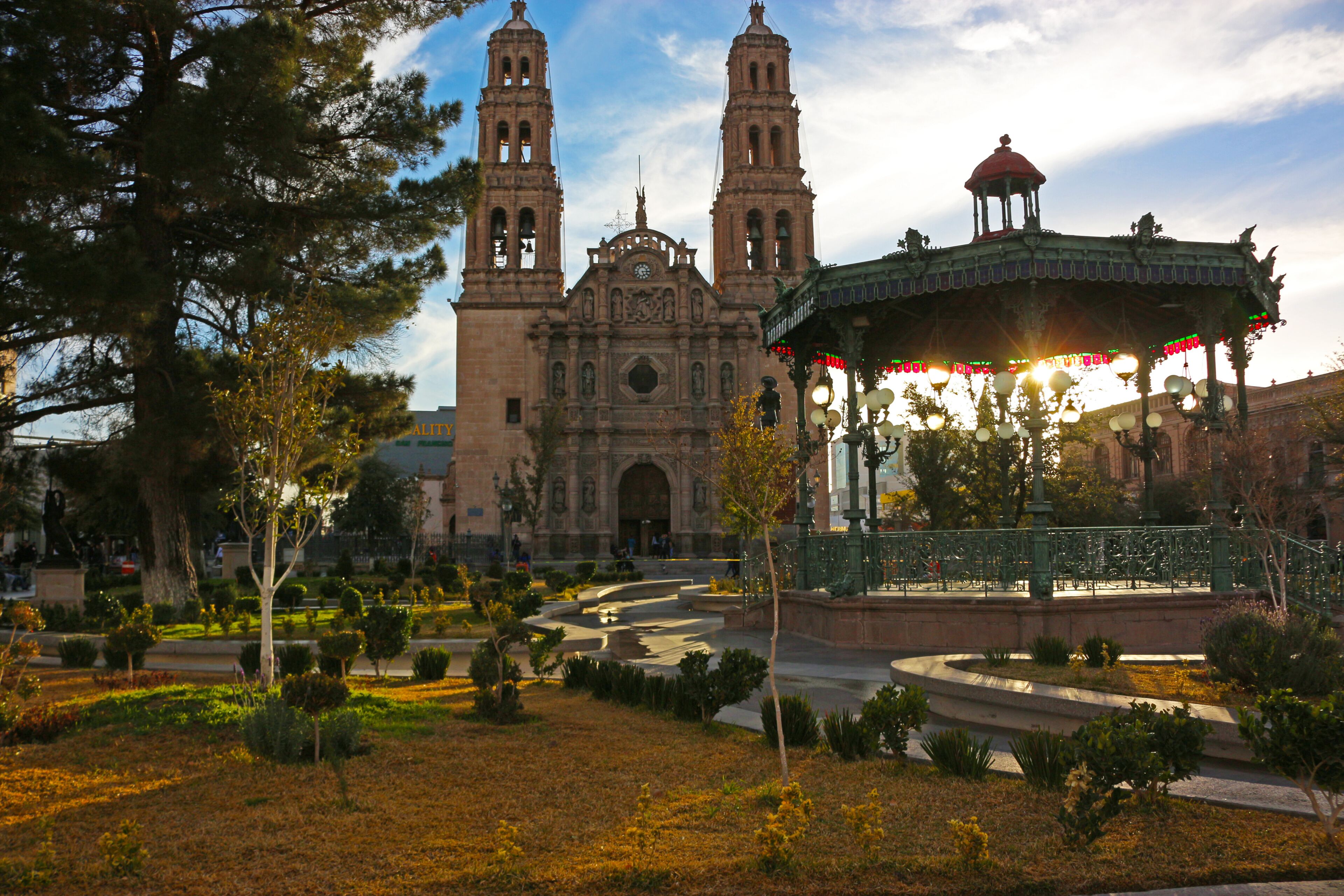 A historic church with two towers, a gazebo, and a well-maintained park with trees and pathways.