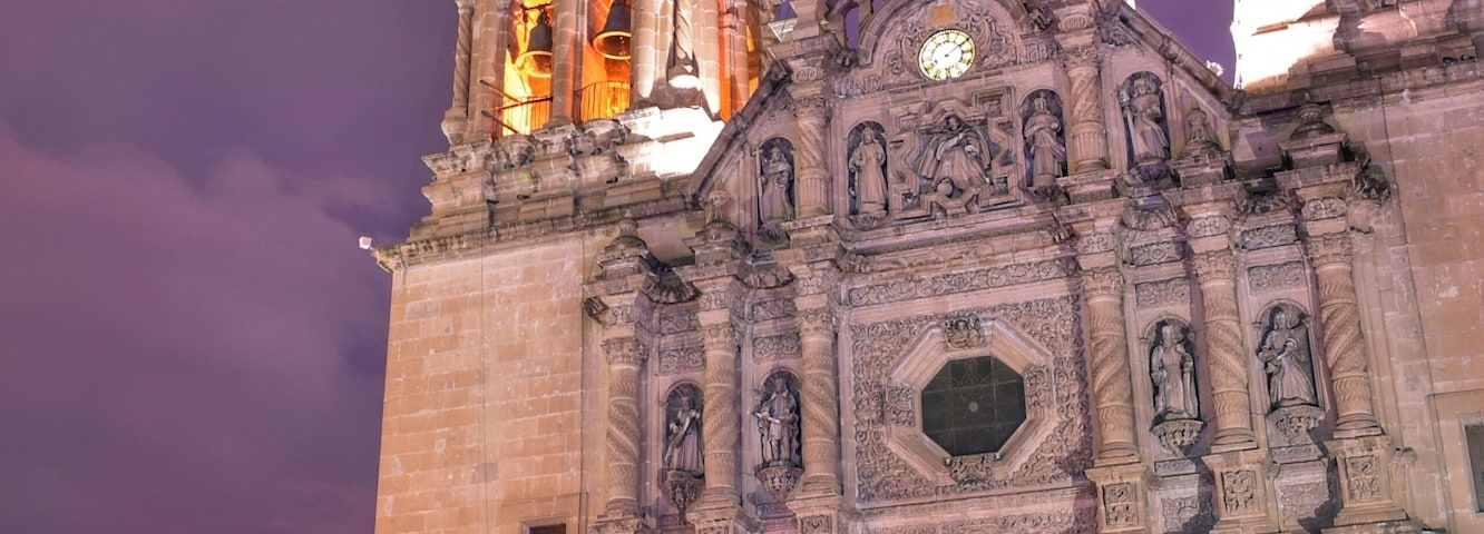Una catedral histórica con dos torres de campanas, fachada ornamentada y una fuente en primer plano.