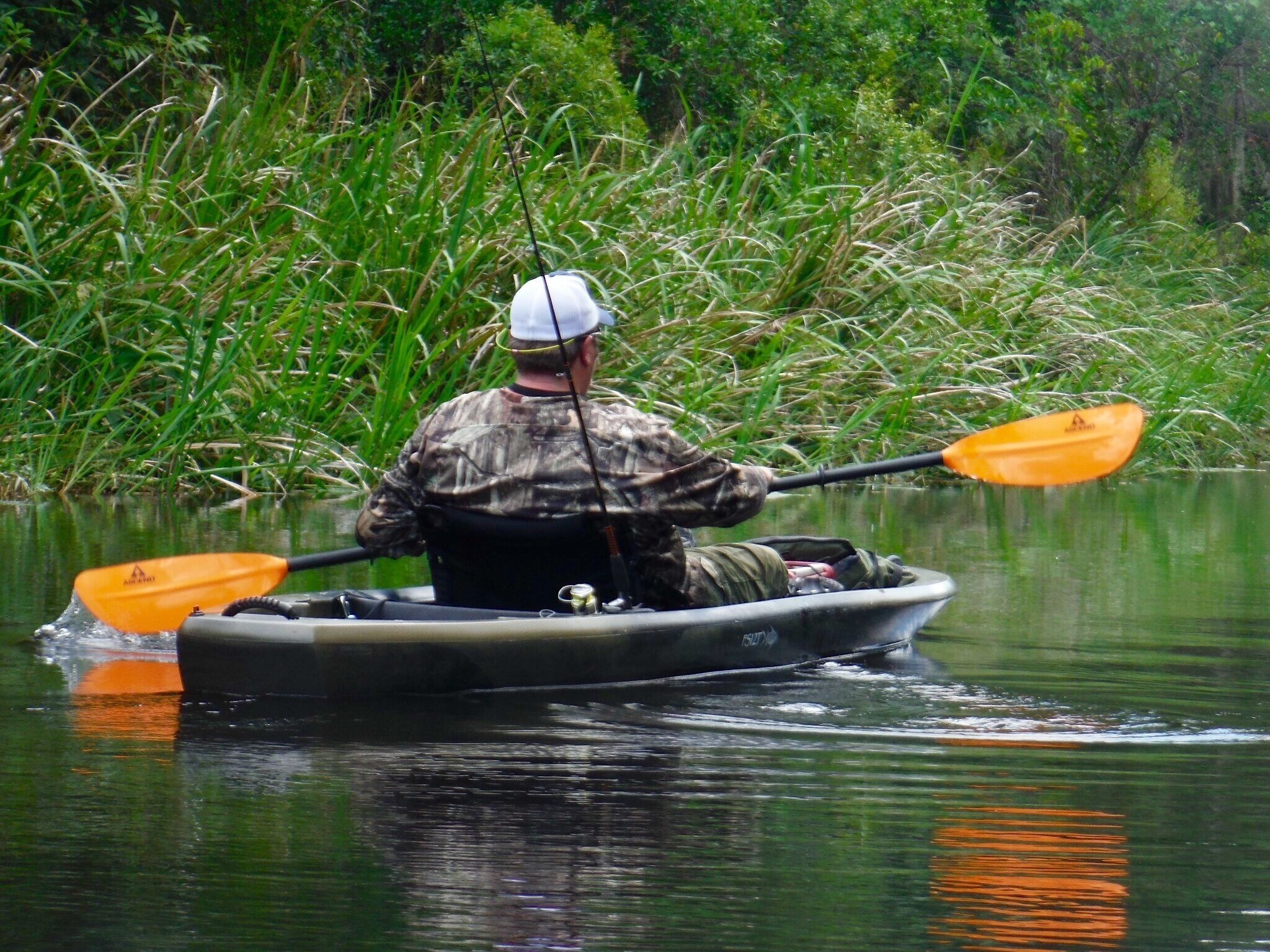 A person in a boat paddling through a calm river surrounded by dense greenery.