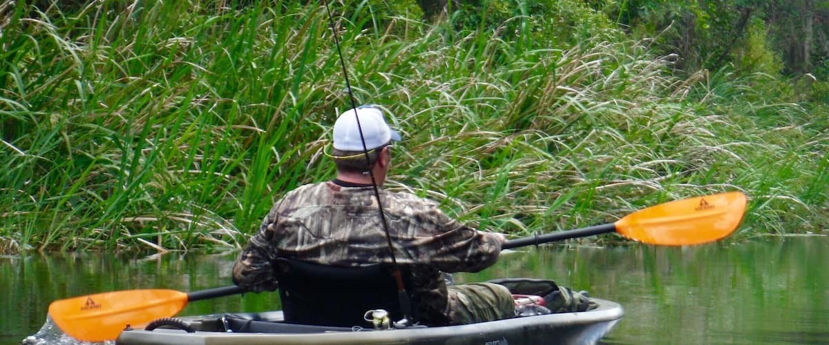 A person in a boat paddling through a calm river surrounded by dense greenery.