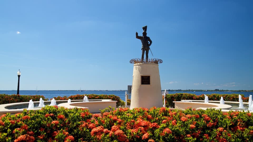 A statue on a pedestal with a fountain in the foreground and a body of water in the background.