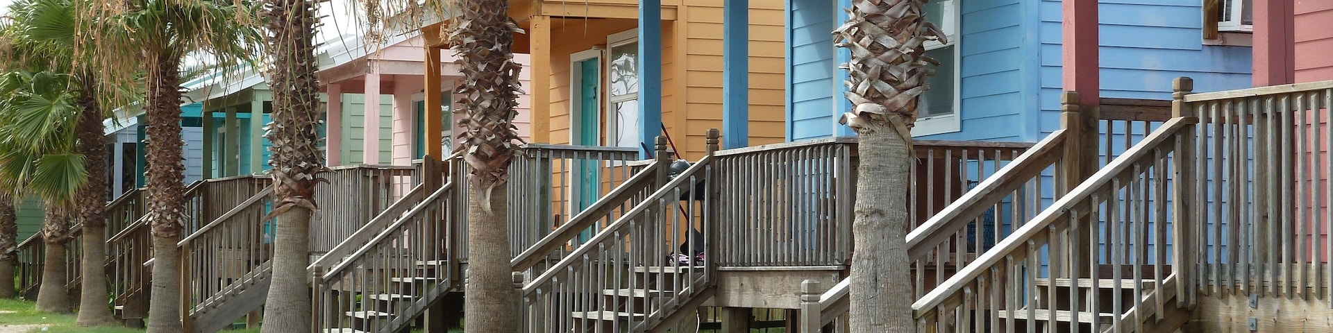 Eine Reihe bunter Strandhäuser mit Holztreppen und Palmen.
