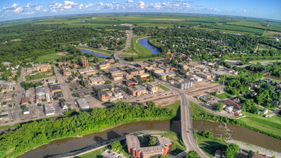 An aerial view of a town with a river, green fields, and a church.