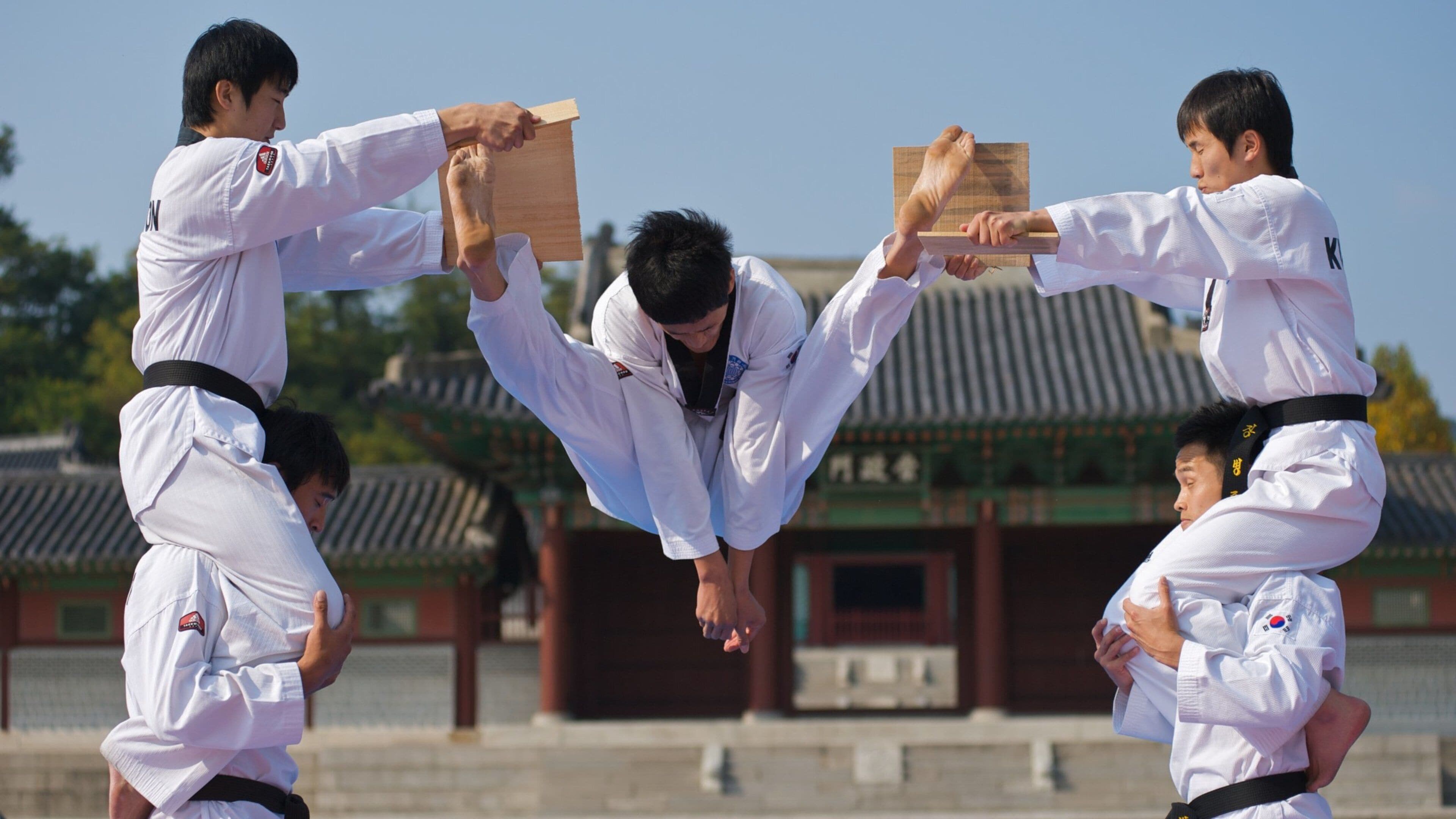 Cuatro personas con uniformes de artes marciales blancas realizando una patada sincronizada.