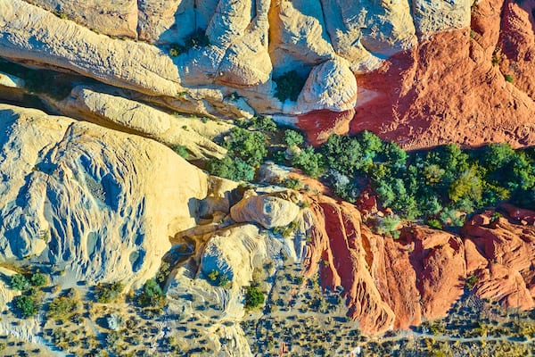 A rugged landscape with layered rock formations, including red and beige cliffs, and sparse green vegetation.
