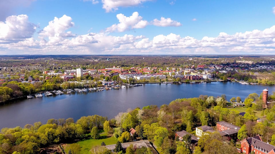 A lakeside town with a prominent church steeple, a marina with boats, and surrounding greenery.