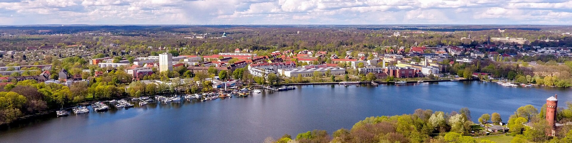A lakeside town with a prominent church steeple, a marina with boats, and surrounding greenery.