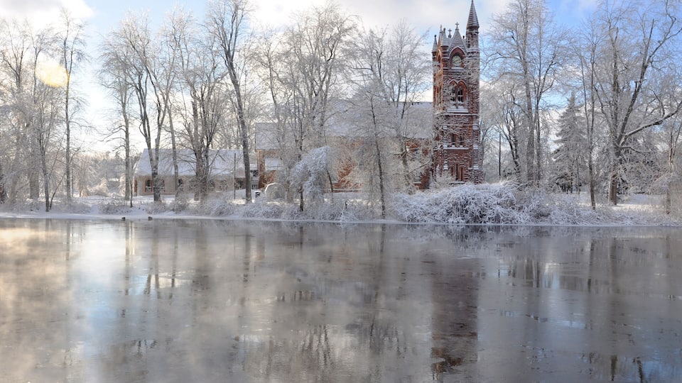 A frozen lake with a church tower and bare trees in the background.