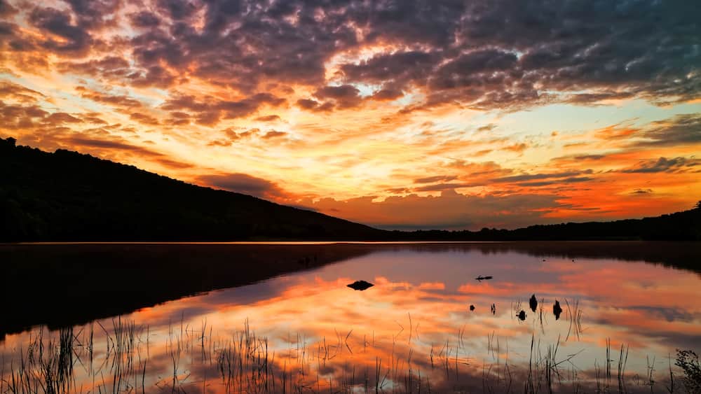 A sunset over a calm lake with reflections of the sky, surrounded by hills.