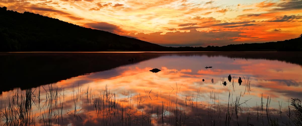 A sunset over a calm lake with reflections of the sky, surrounded by hills.