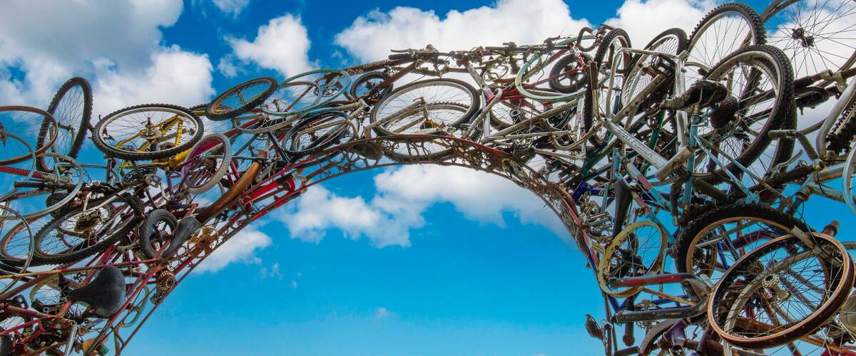 A large number of bicycles arranged in an arch against a blue sky with clouds.