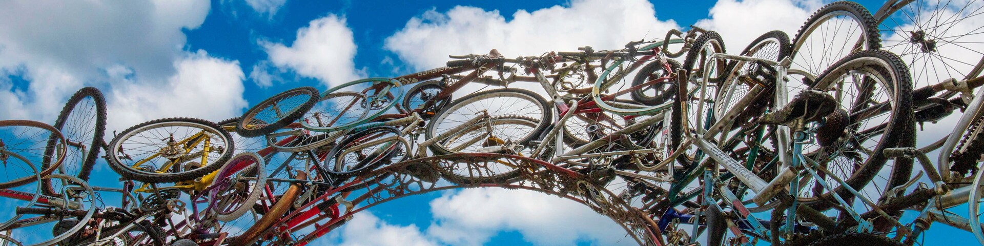 A large number of bicycles arranged in an arch against a blue sky with clouds.