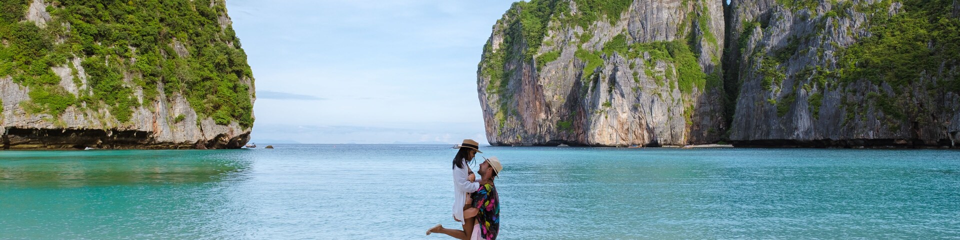 A beach with clear turquoise water, white sand, and large limestone cliffs.