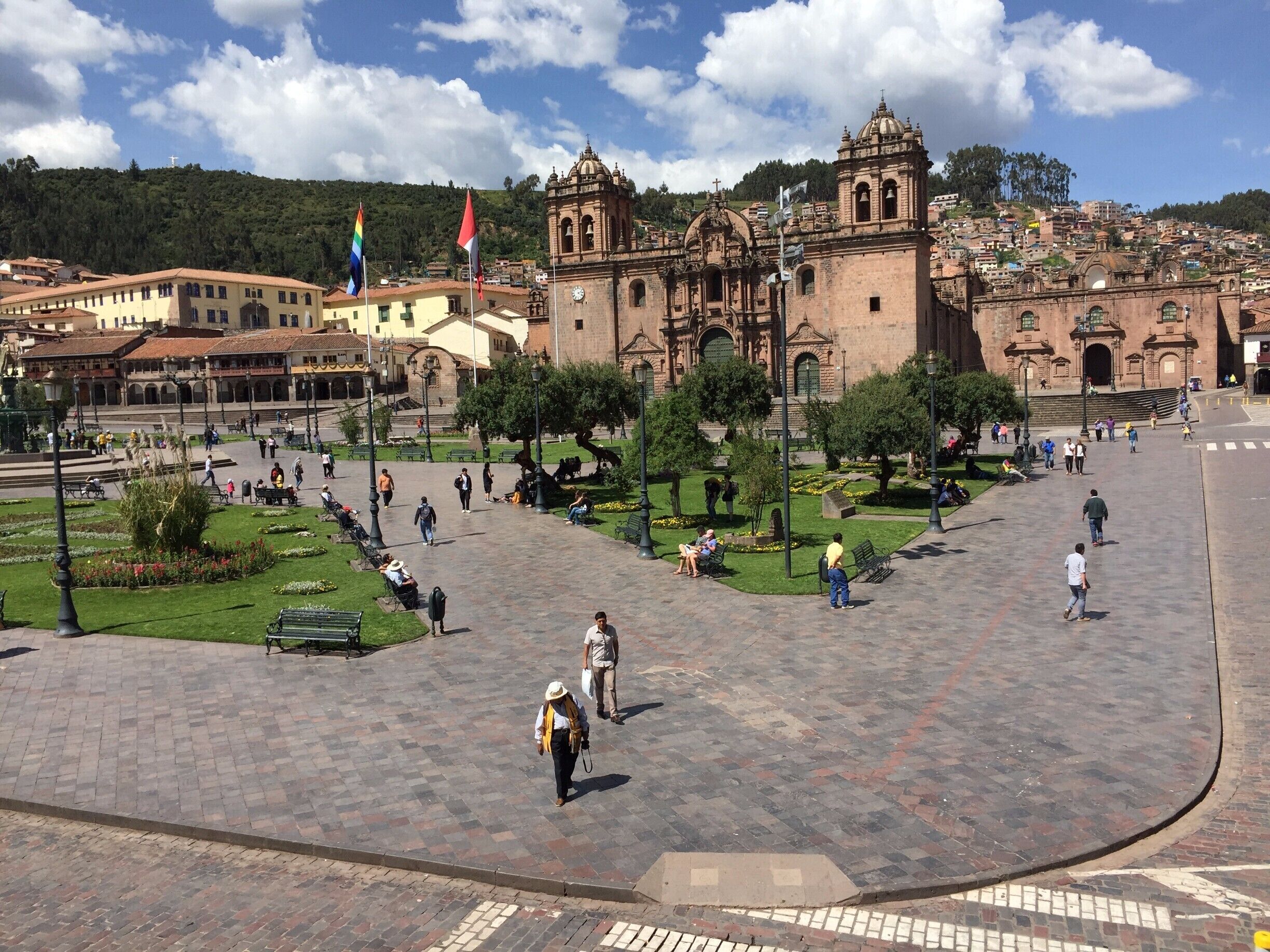 Una plaza con una iglesia histórica, gente caminando y banderas.