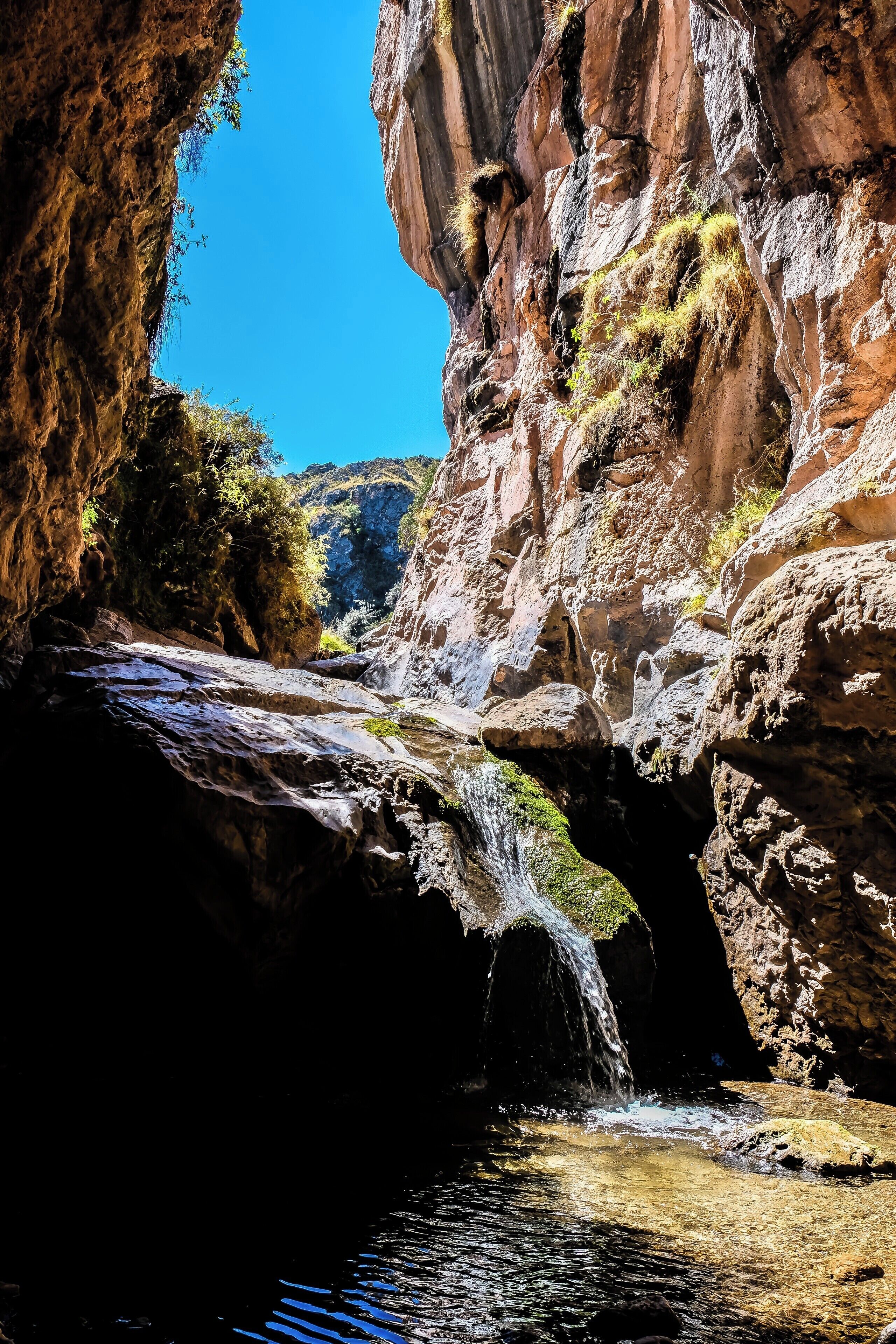 Una cascada que se precipita por un desfiladero rocoso bajo un cielo azul despejado.