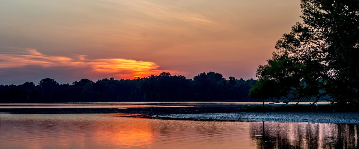 A calm lake at sunset with a reflection of the sky and trees.