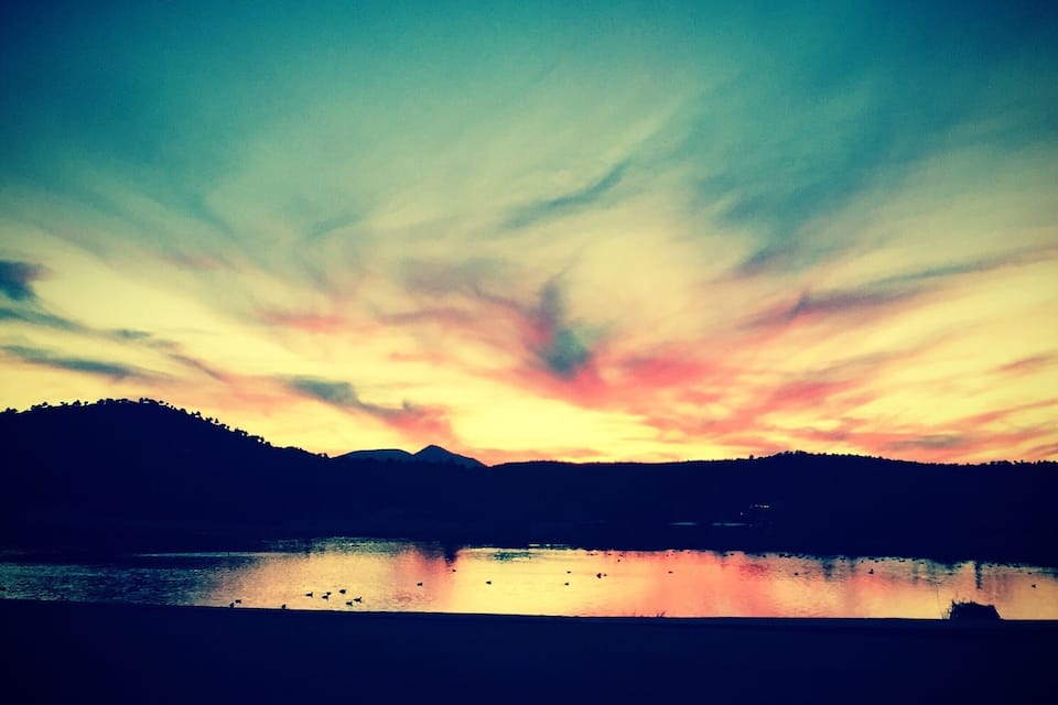 Un atardecer sobre un lago con montañas al fondo.