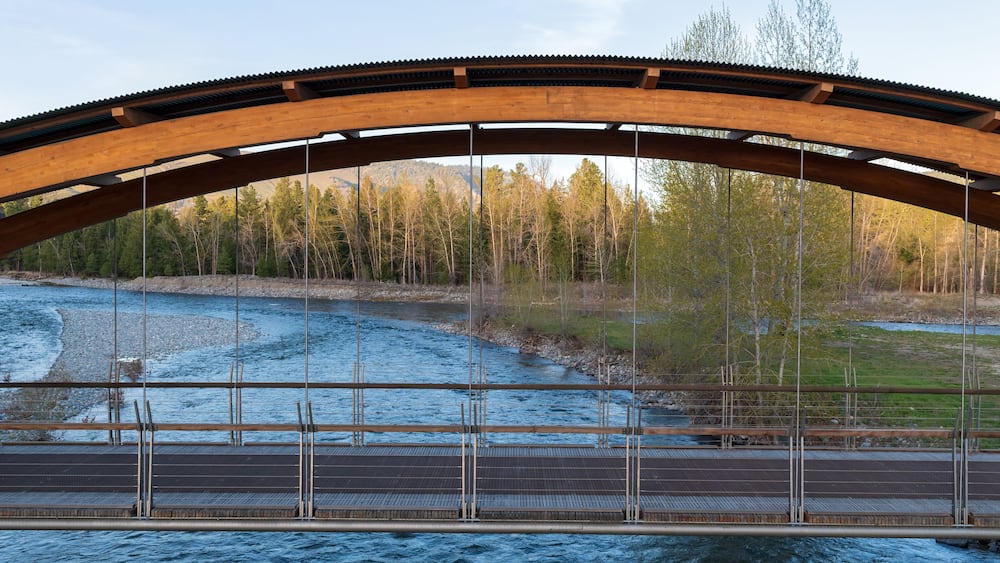 A wooden bridge over a river with a forested hillside in the background.