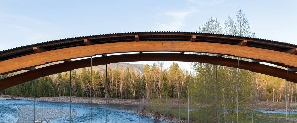 Un pont en bois enjambant une rivière, avec une colline boisée en arrière-plan.