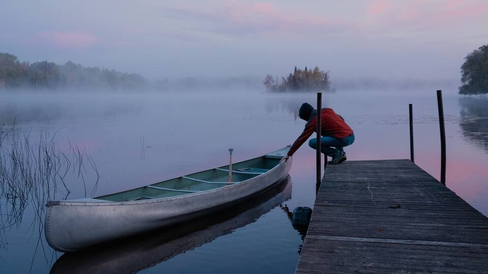 A misty lake with a wooden dock and a canoe.