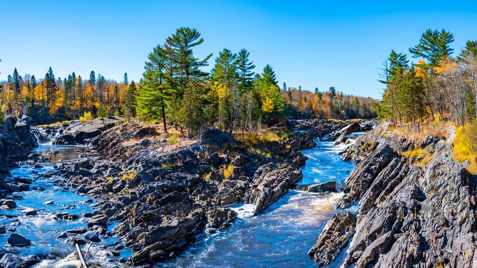 A river flowing through a rocky gorge with autumn-colored trees.