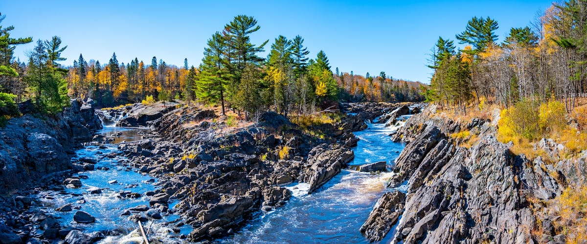 A river flowing through a rocky gorge with autumn-colored trees.