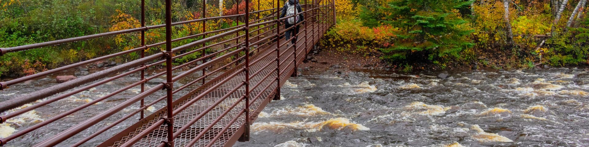 Woman hiking across suspension bridge over river