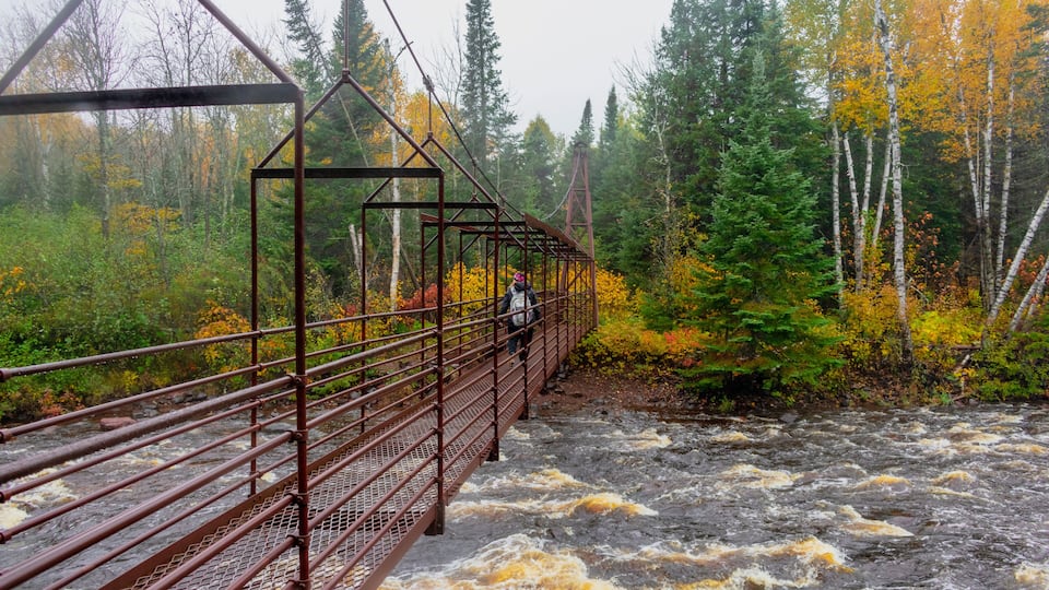 A metal bridge over a fast-flowing river surrounded by autumn-colored trees.