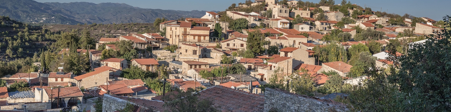 Un village perché sur une colline, avec des toits de tuiles rouges et des bâtiments en pierre, entouré de montagnes et de verdure.