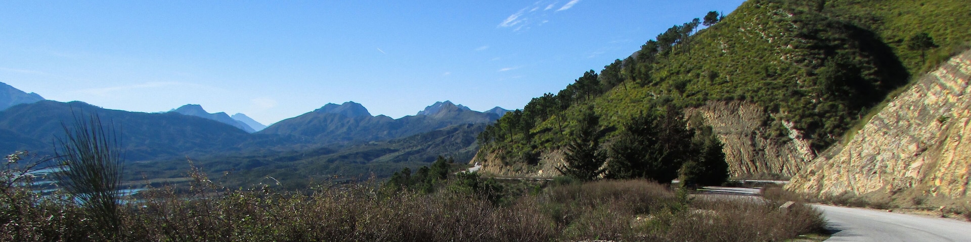 A winding mountain road with a clear blue sky and distant mountains.