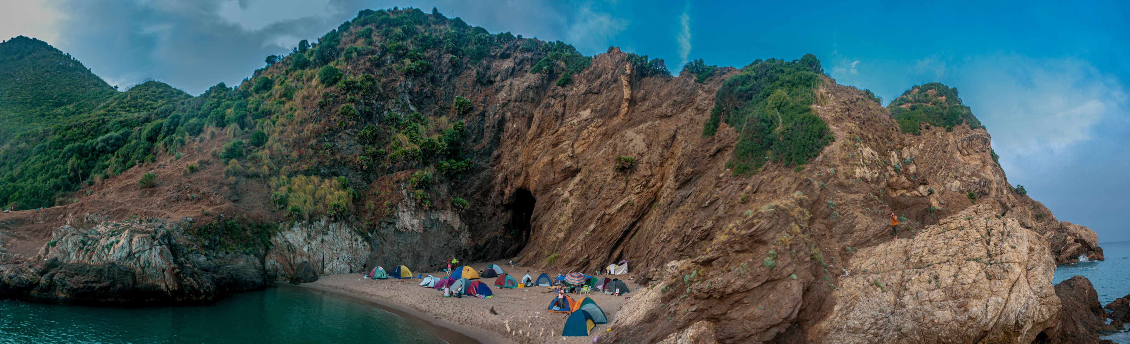 A rocky coastline with tents set up along the shore.