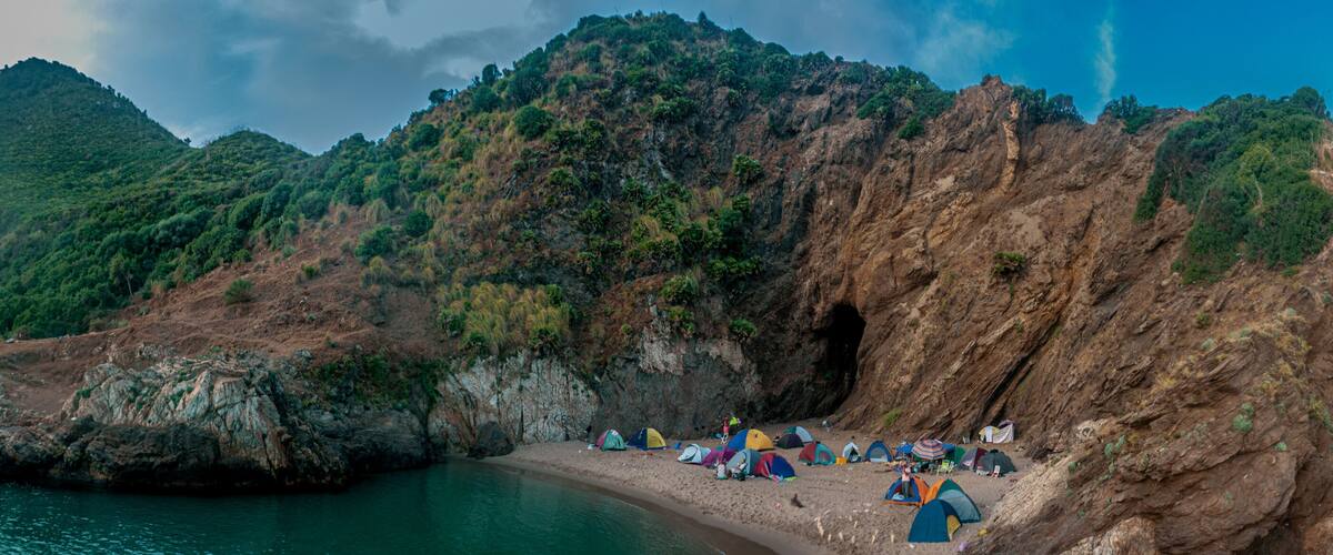 A rocky coastline with tents set up along the shore.