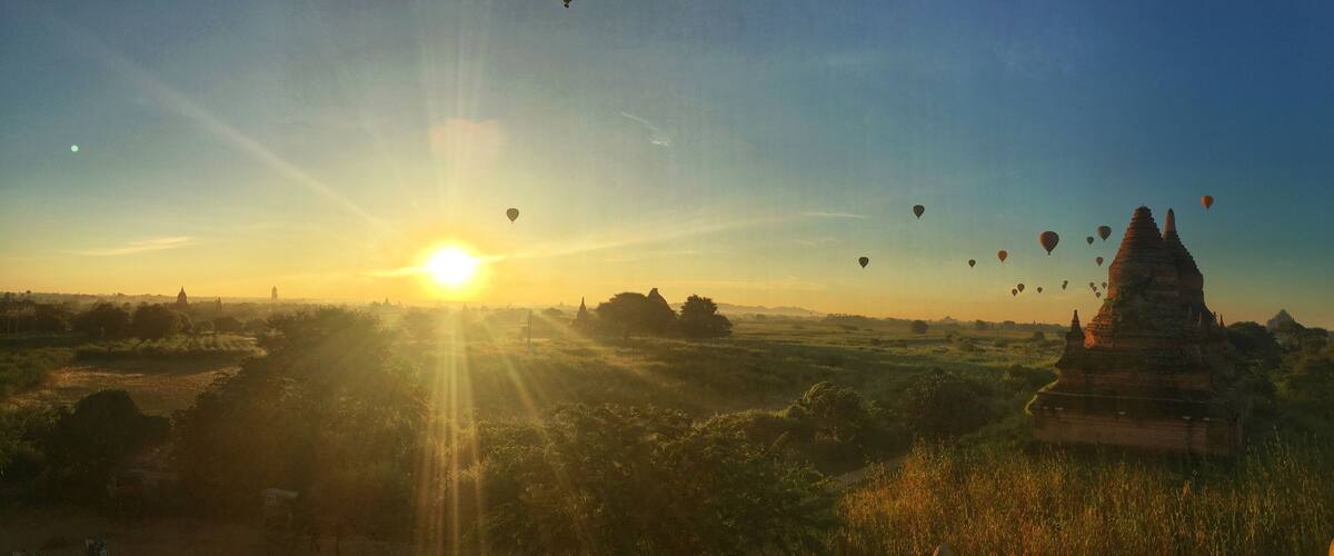 A sunset over a landscape with hot air balloons and ancient temple structures.