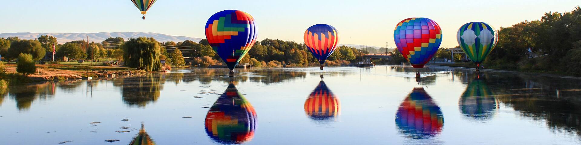 Dawn ascent of vibrant balloons over water