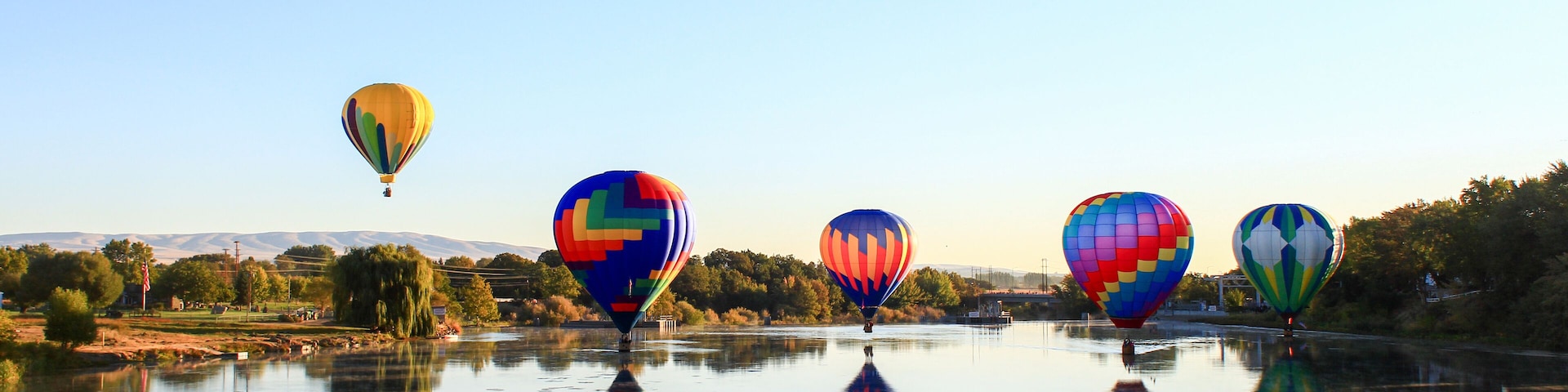 Dawn ascent of vibrant balloons over water