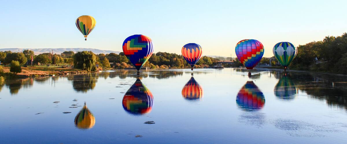 A calm river with reflections of colorful hot air balloons.