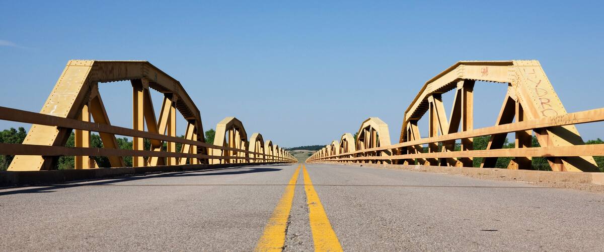 A bridge with yellow railings and a cracked road surface.
